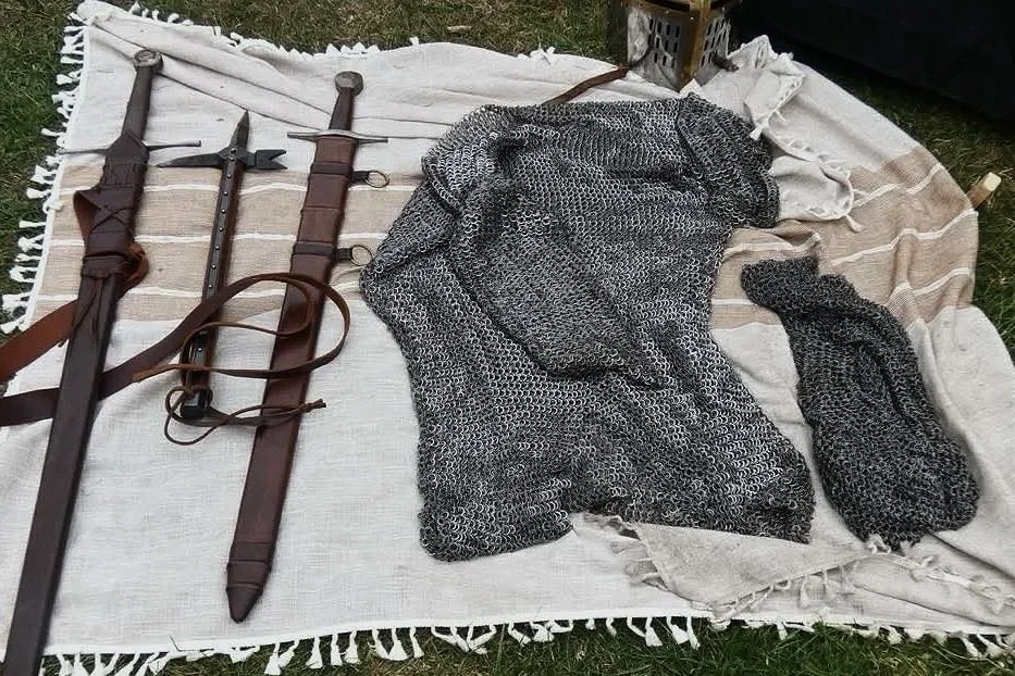 Historical swords and chainmail armor laid out on a blanket.