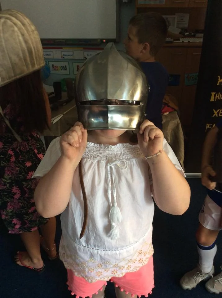 Child wearing a knight helmet toy in a classroom or play area.