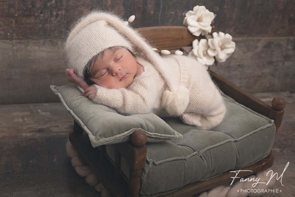 bébé endormi vêtu de laine blanche avec un petit bonnet sur un lit en bois