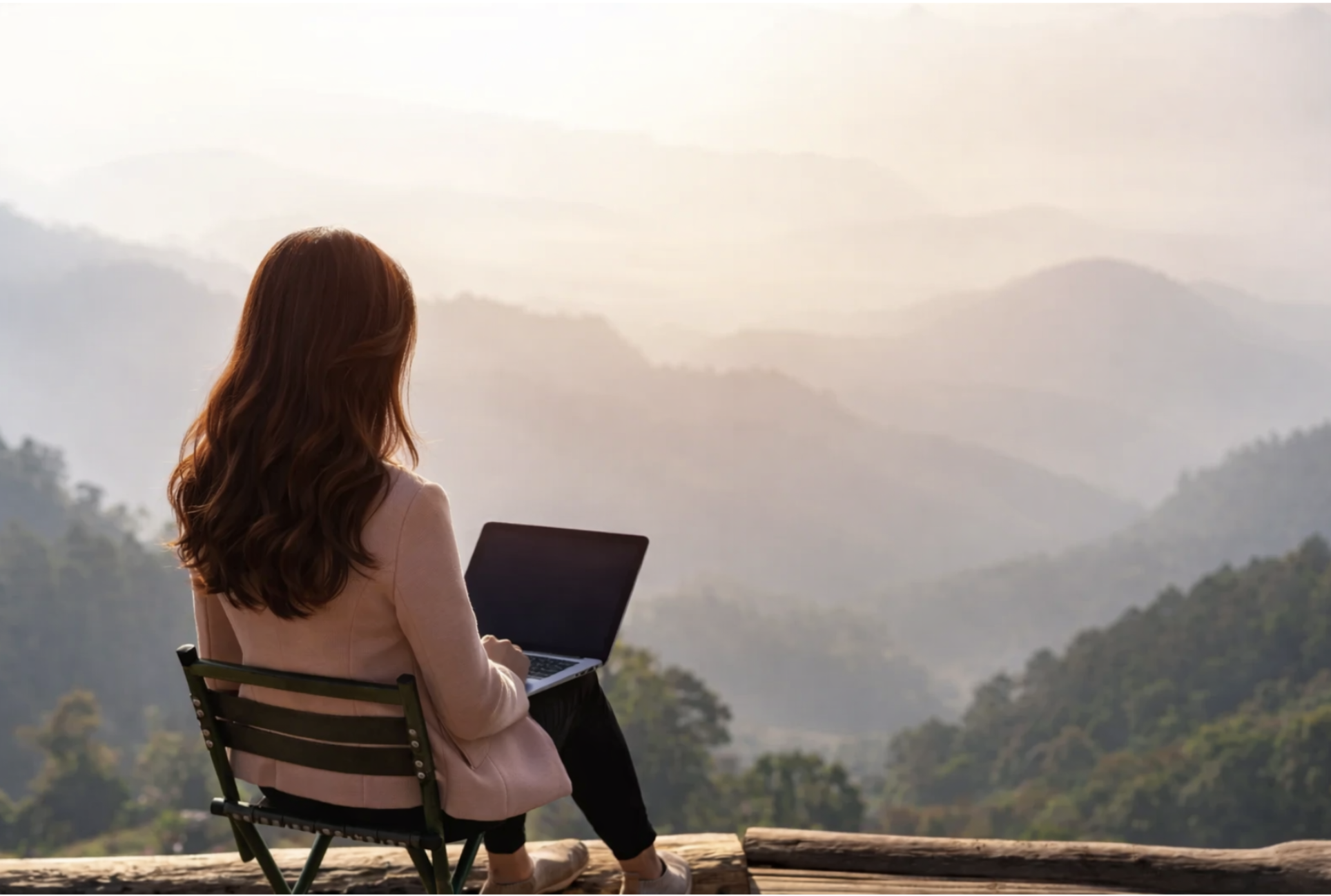 Woman working on laptop overlooking mountains, representing remote BodyTalk and mind-body health sessions from home