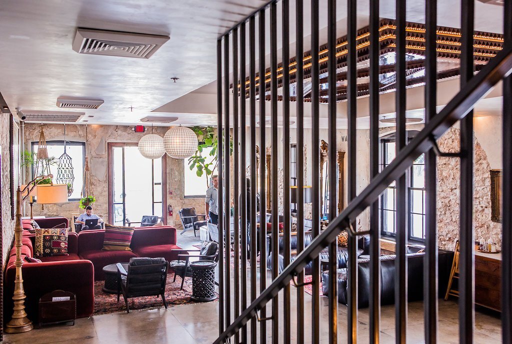Interior of a cozy living room with red sofas, black chairs, hanging white paper lanterns, large windows, potted plants, and wooden accents separated by black metal bars.
