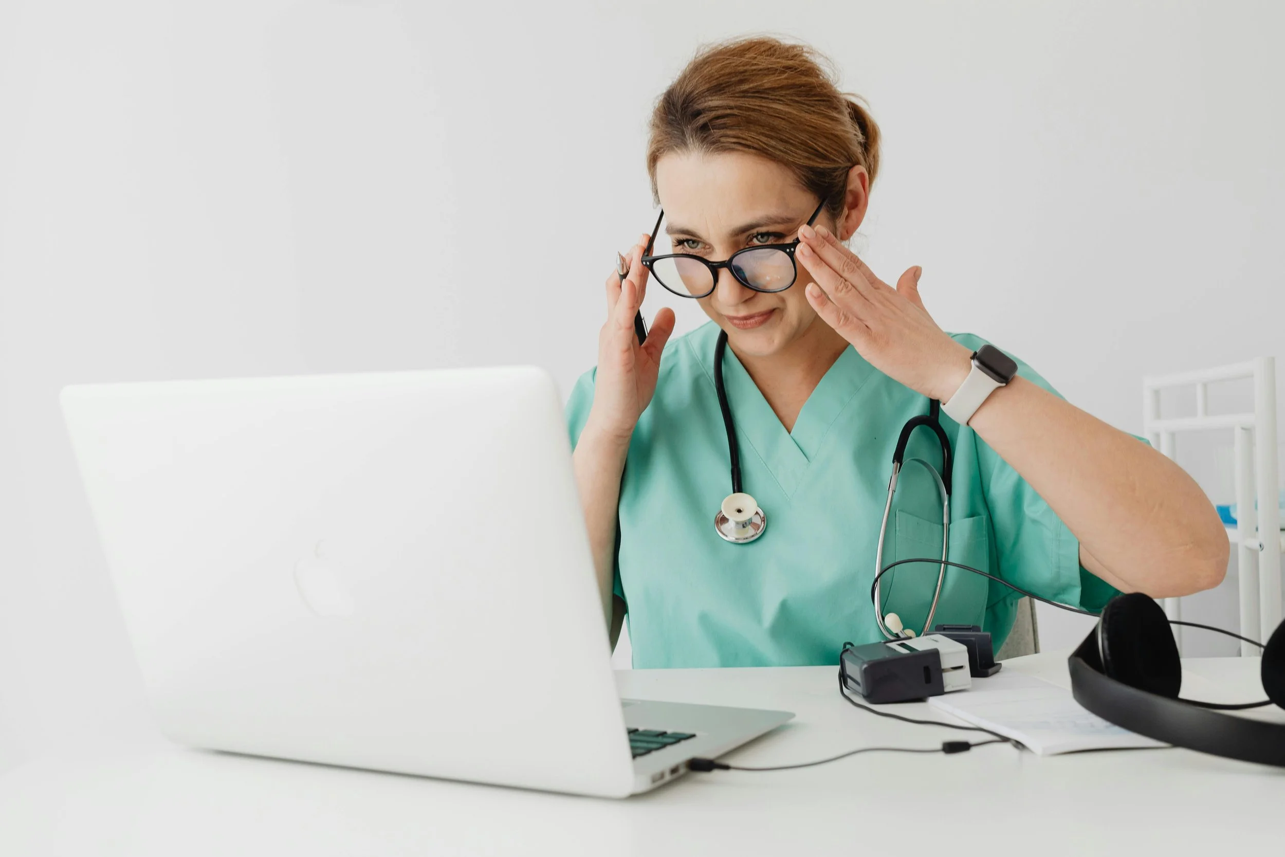 Female practice owner in light green scrubs working at her desk in a modern clinic, symbolizing premium medical branding and leadership.