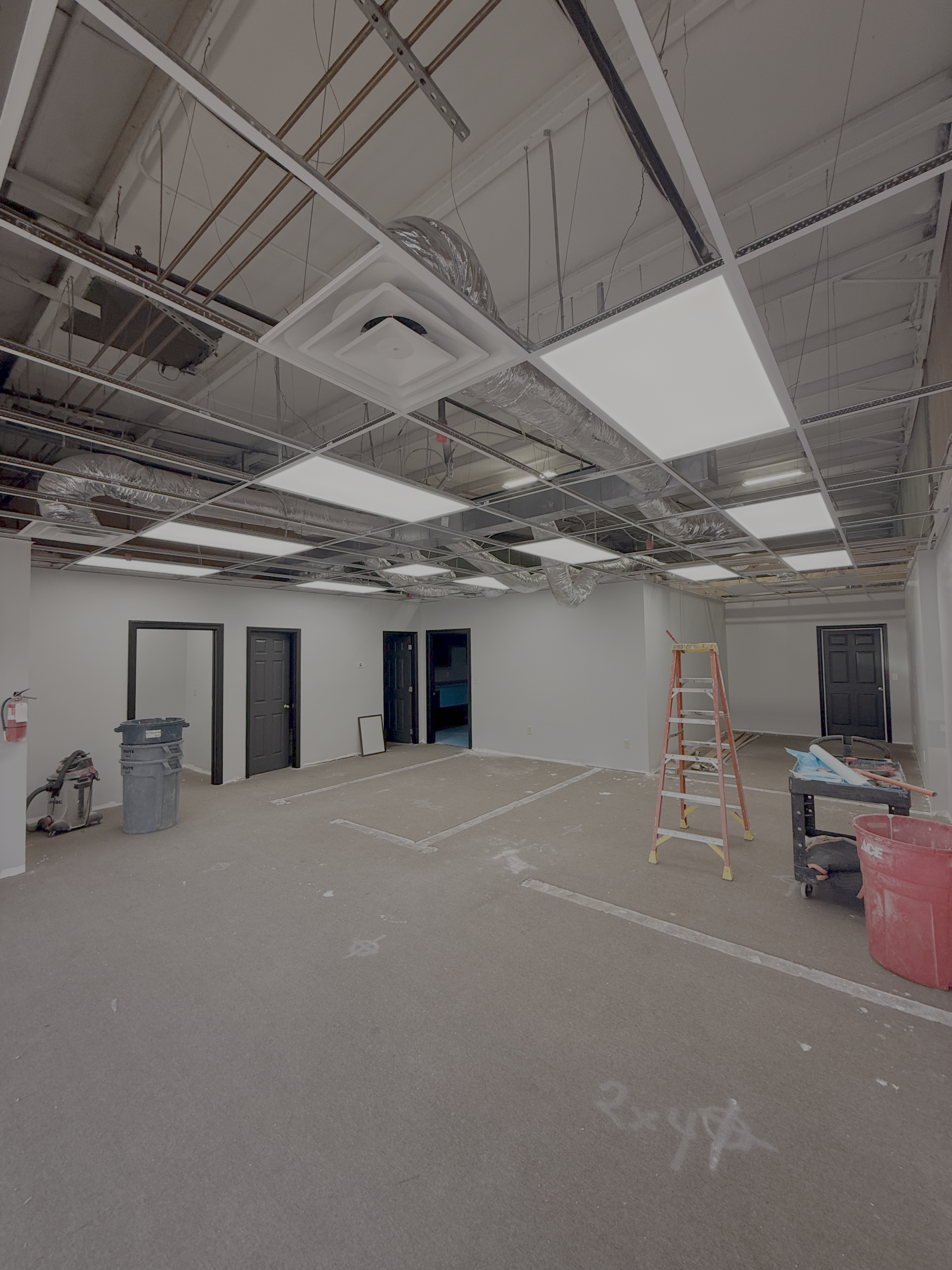 Construction site indoor with a partially finished ceiling, scaffolding, ladders, and construction materials on the floor.