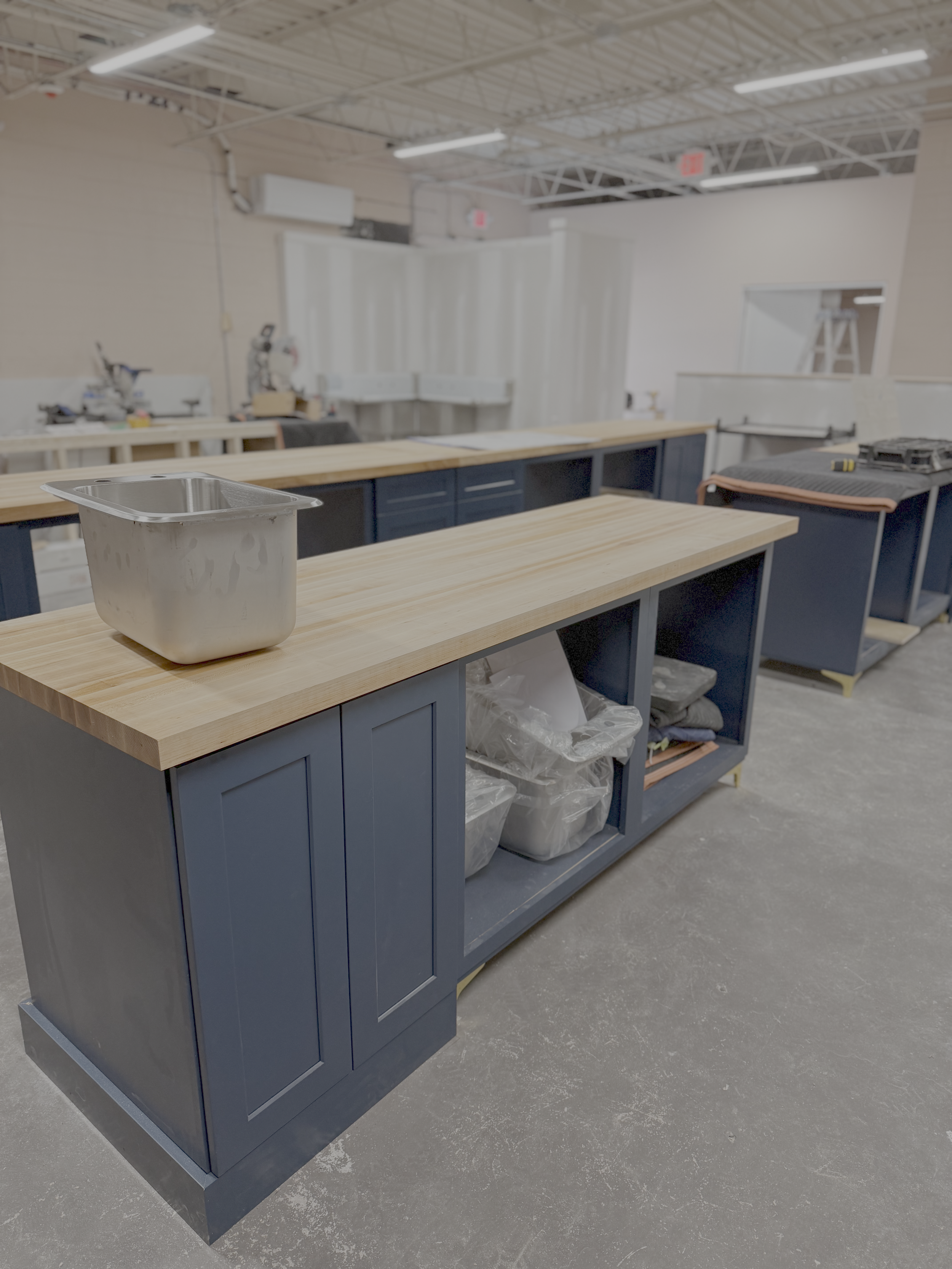 Interior of a workshop or fabrication space with a large blue cabinet, a wooden countertop, and various tools and equipment in the background.