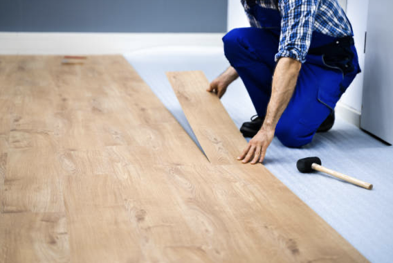 Person installing wooden flooring with a hand saw nearby.