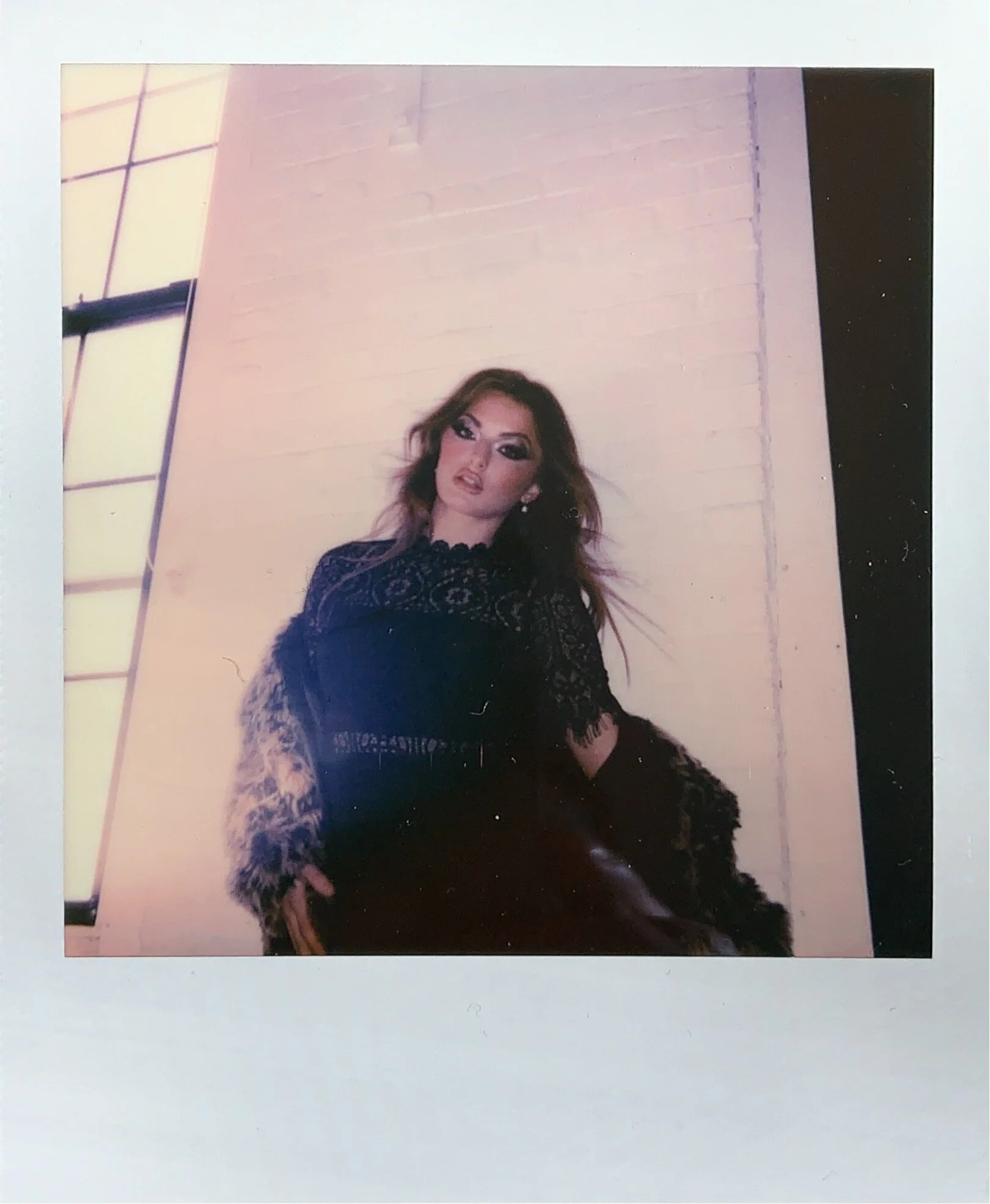 Person wearing a dark, stylish outfit with lace details standing indoors next to a large window.