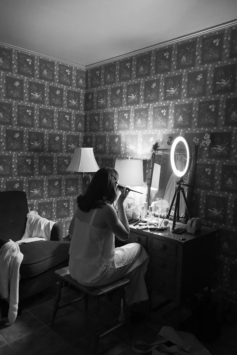 Black and white photo of a groom getting ready in a room with charming wallpaper for a micro wedding in North Carolina