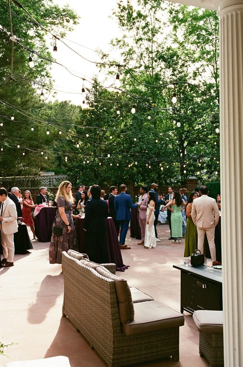 Guests mingling outside with string lights overhead at a reception at The Matthews House in Cary, NC.