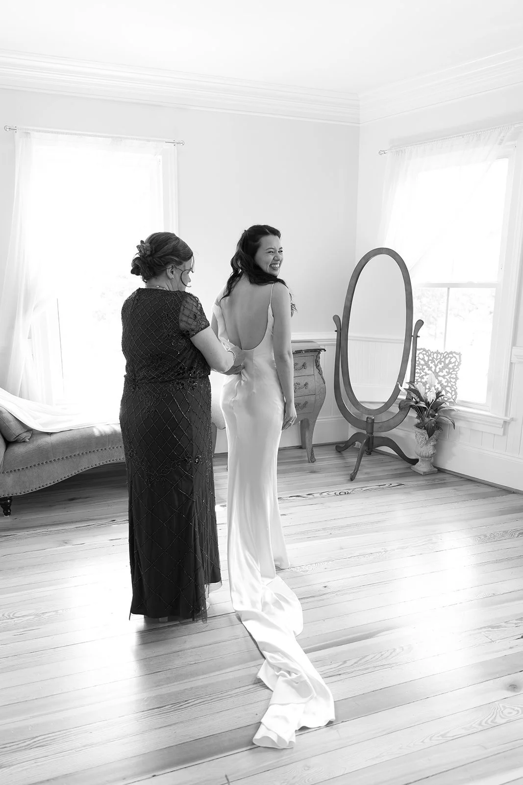 Black and white photo of bride putting dress on with mom’s help at The Matthews House in Cary.