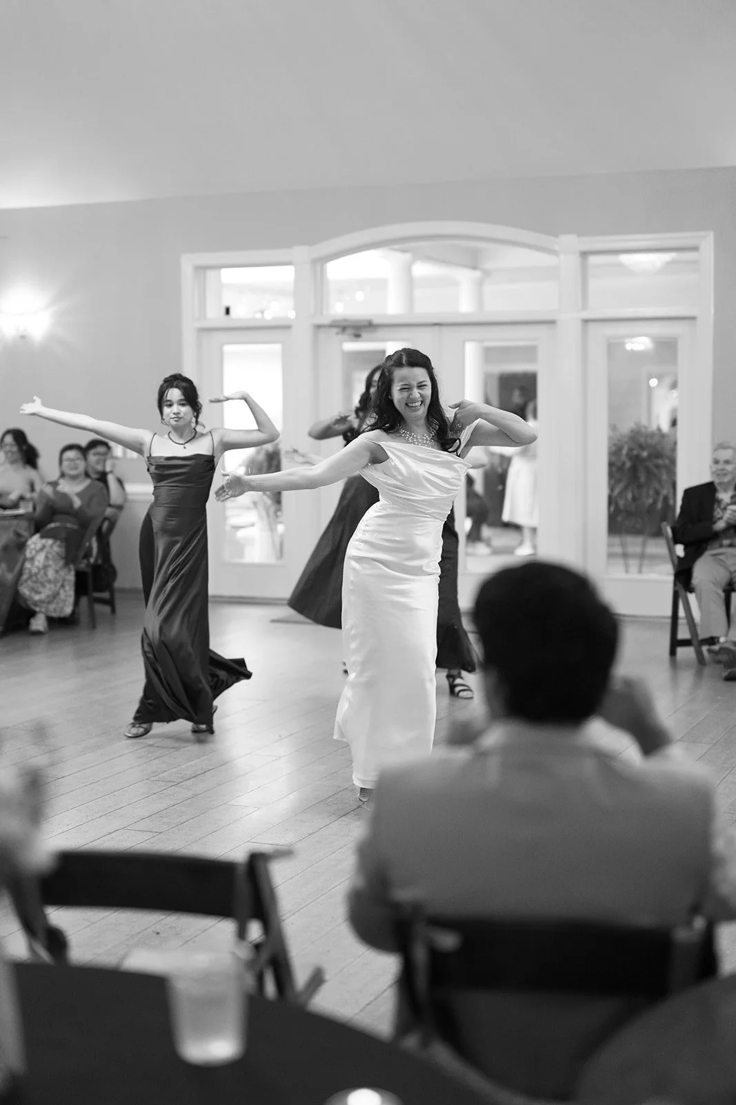 Black and white photo of bride doing a surprise dance with her bridesmaids for the groom inside The Matthews House in Cary.
