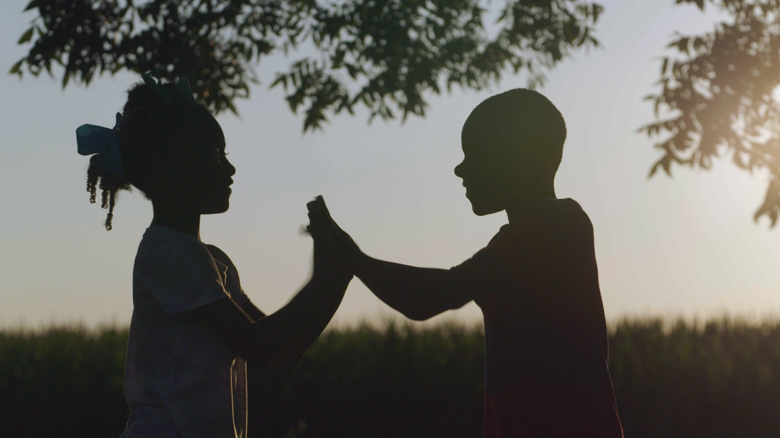 Two silhouetted children play outdoors