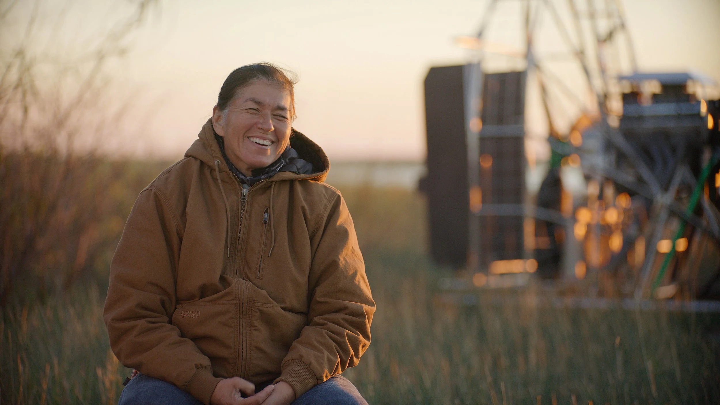 A person in a brown zip-up sits outside, laughing