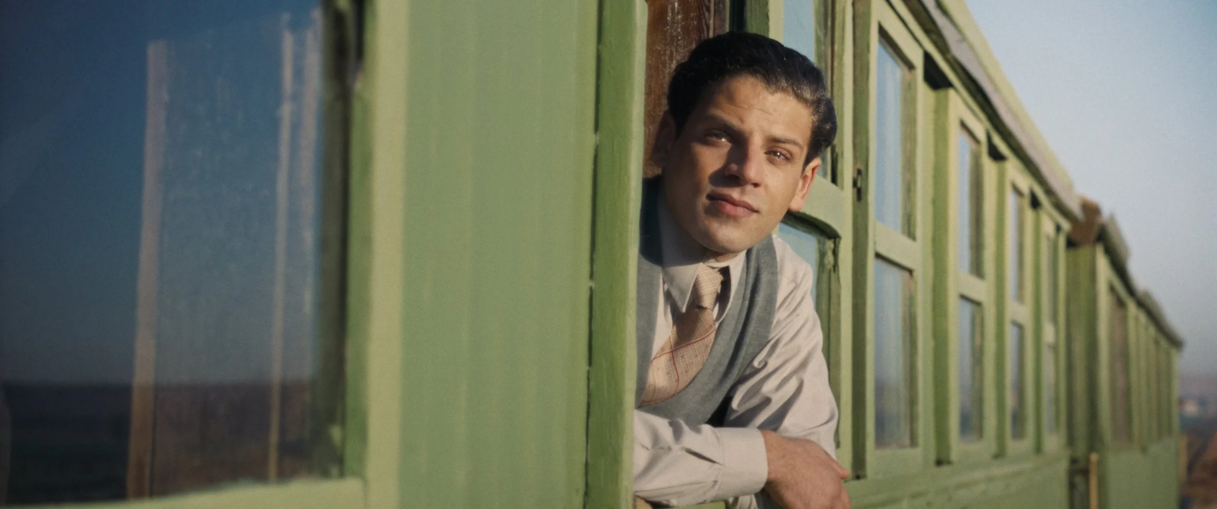 A man leans out of a green train car, tears in his eyes