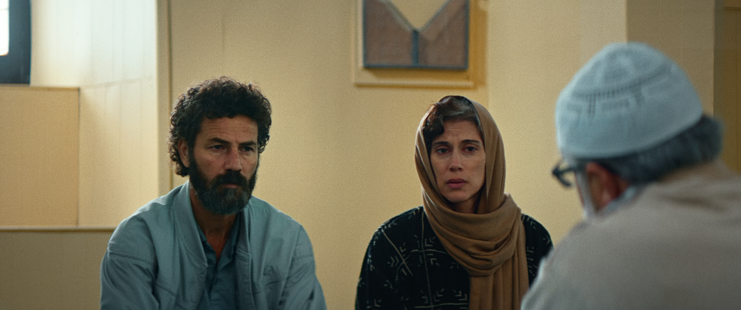 A frame from the film All That's Left Of You showing a man and a woman listening to a pious man.