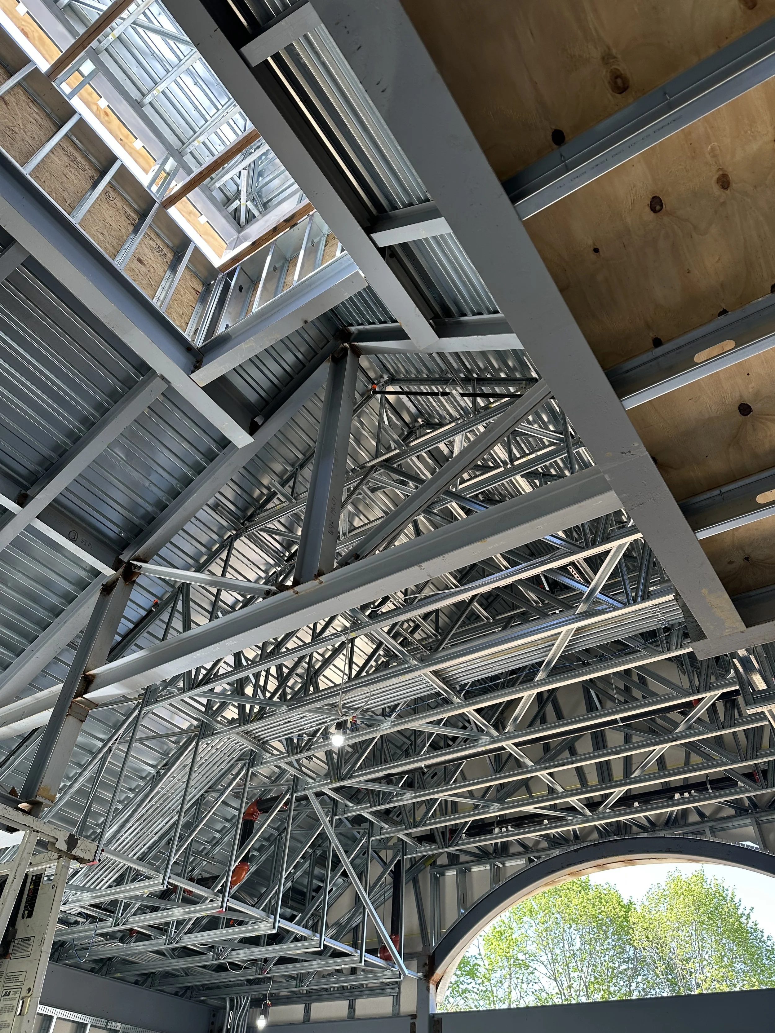 This interior shot looks straight up into the soaring ceiling of the library addition, showcasing a complex web of silver steel trusses and beams. Large industrial-grade girders provide the main support, while a dense network of lighter metal cross-b