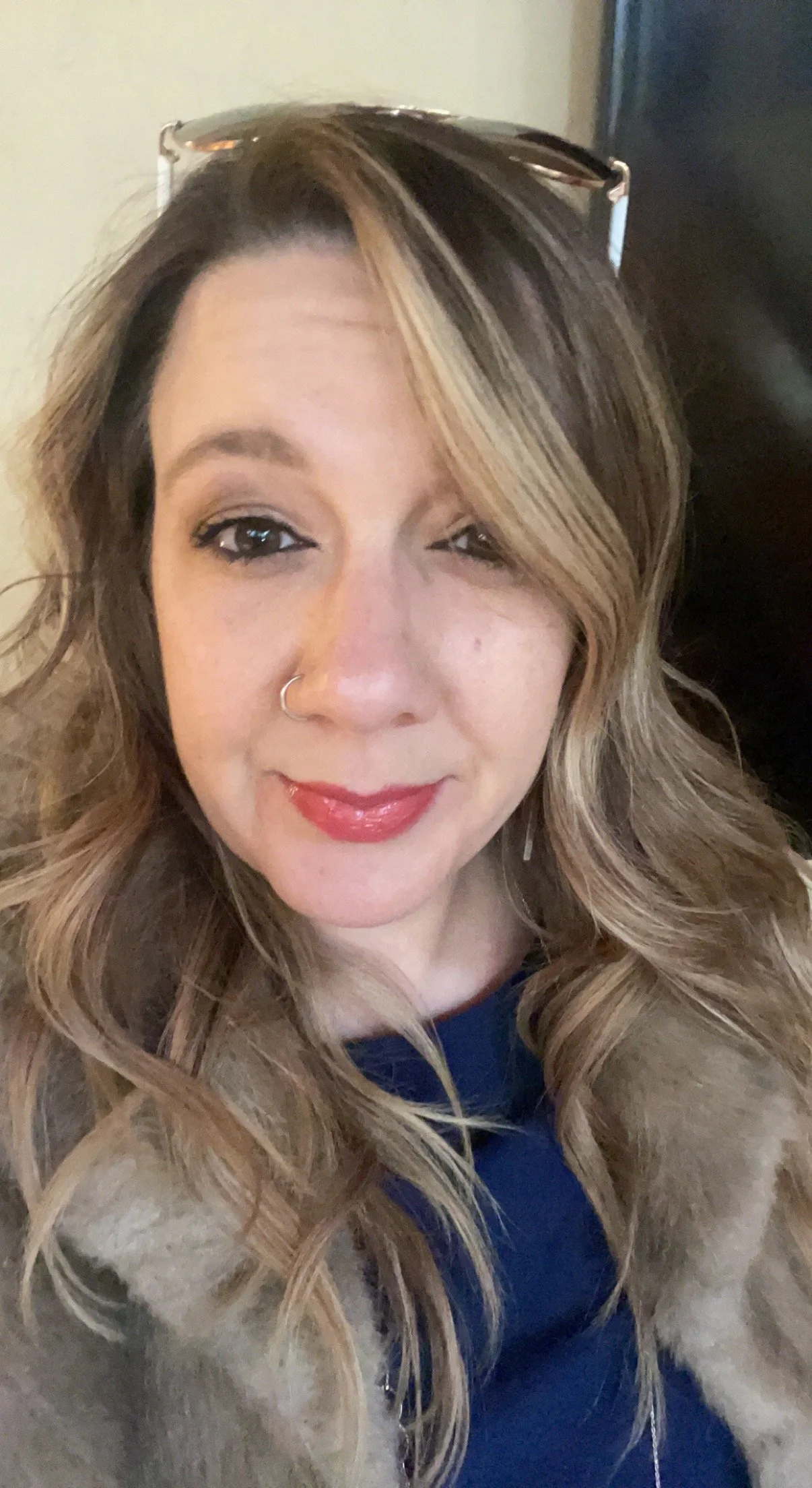 Woman with long wavy hair and nose ring smiling at the camera.