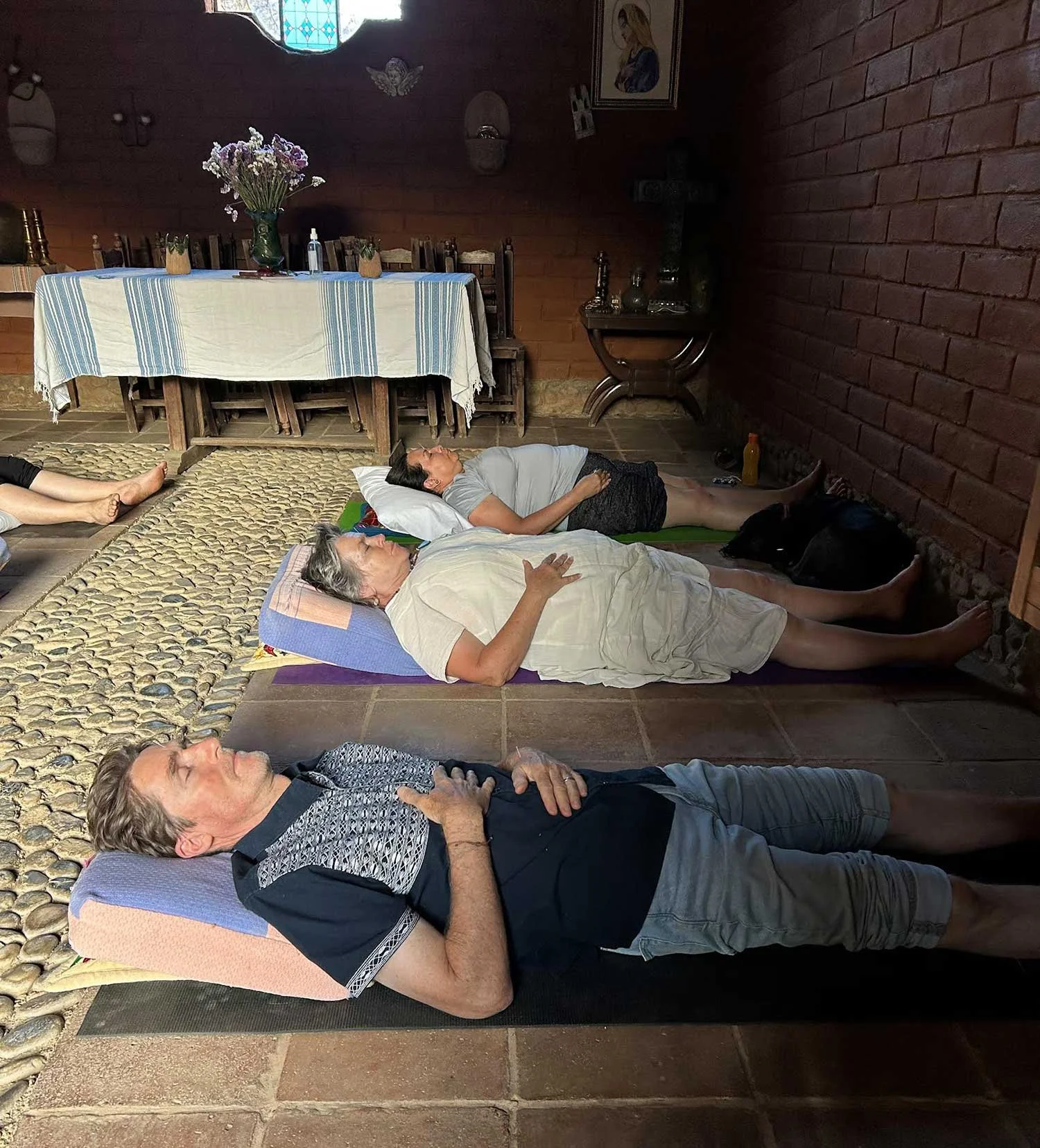 People lying down on yoga mats and blankets in a room, possibly participating in a meditation or relaxation session.