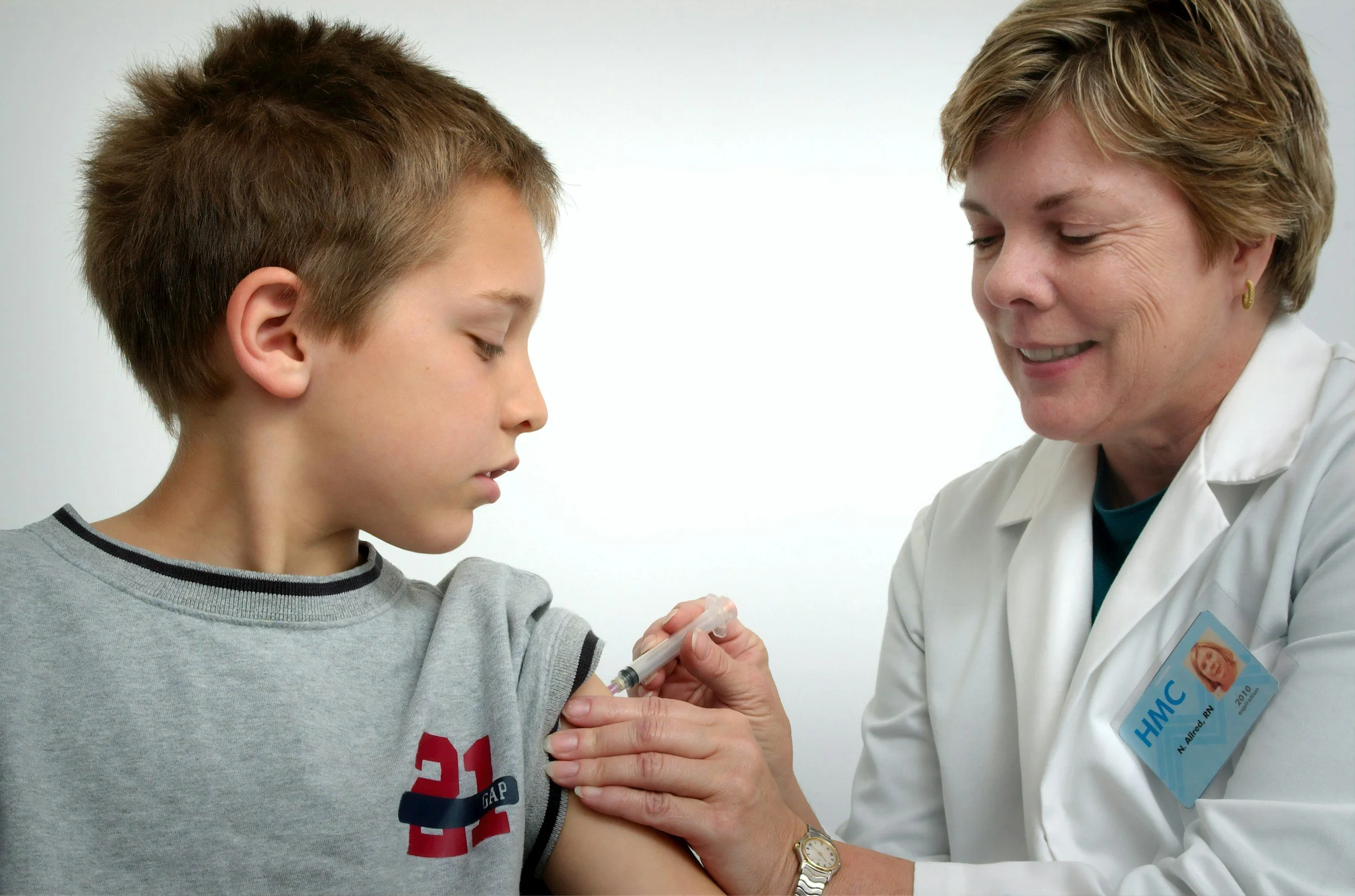 A young boy looks away while a healthcare worker gives him a vaccine shot in his upper arm.