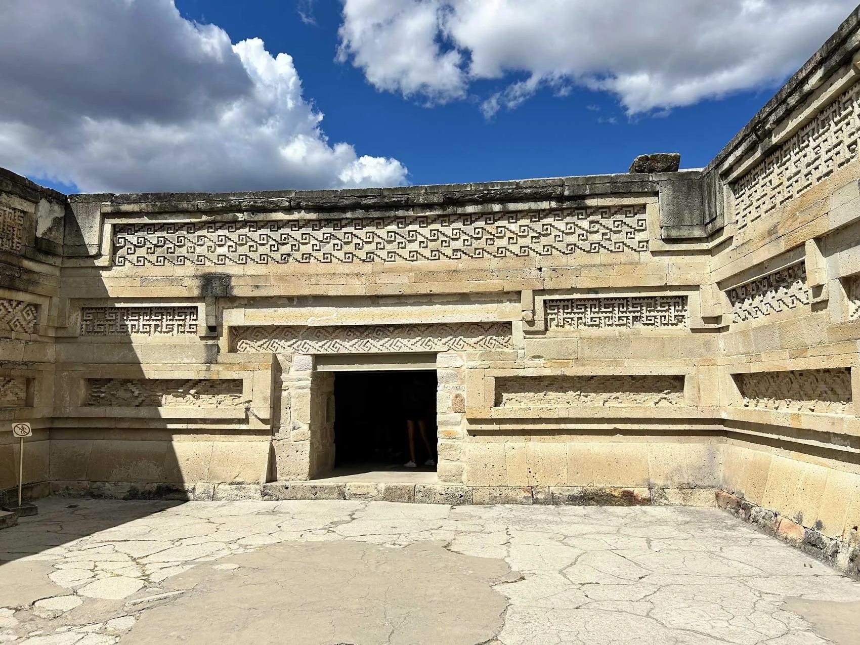 Ancient stone structure with intricate geometric carvings on the upper walls and an open doorway in the center, set against a partly cloudy sky.