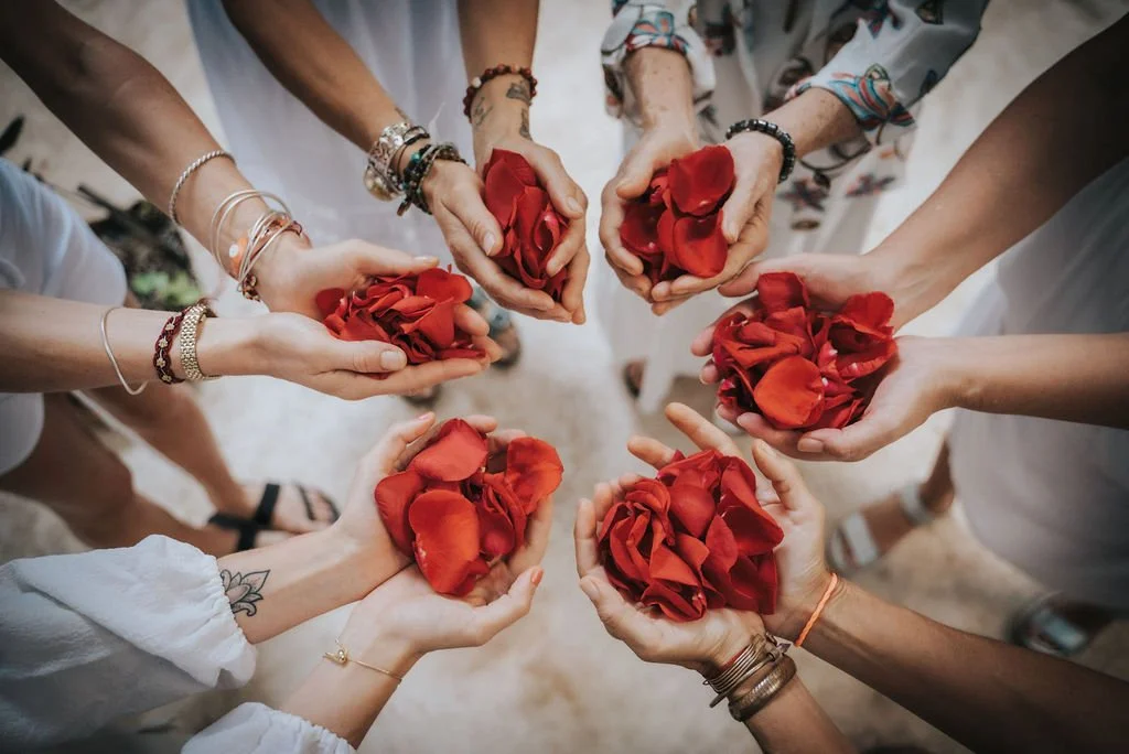 Several people holding small bags of red rose petals in a circle, seen from above.