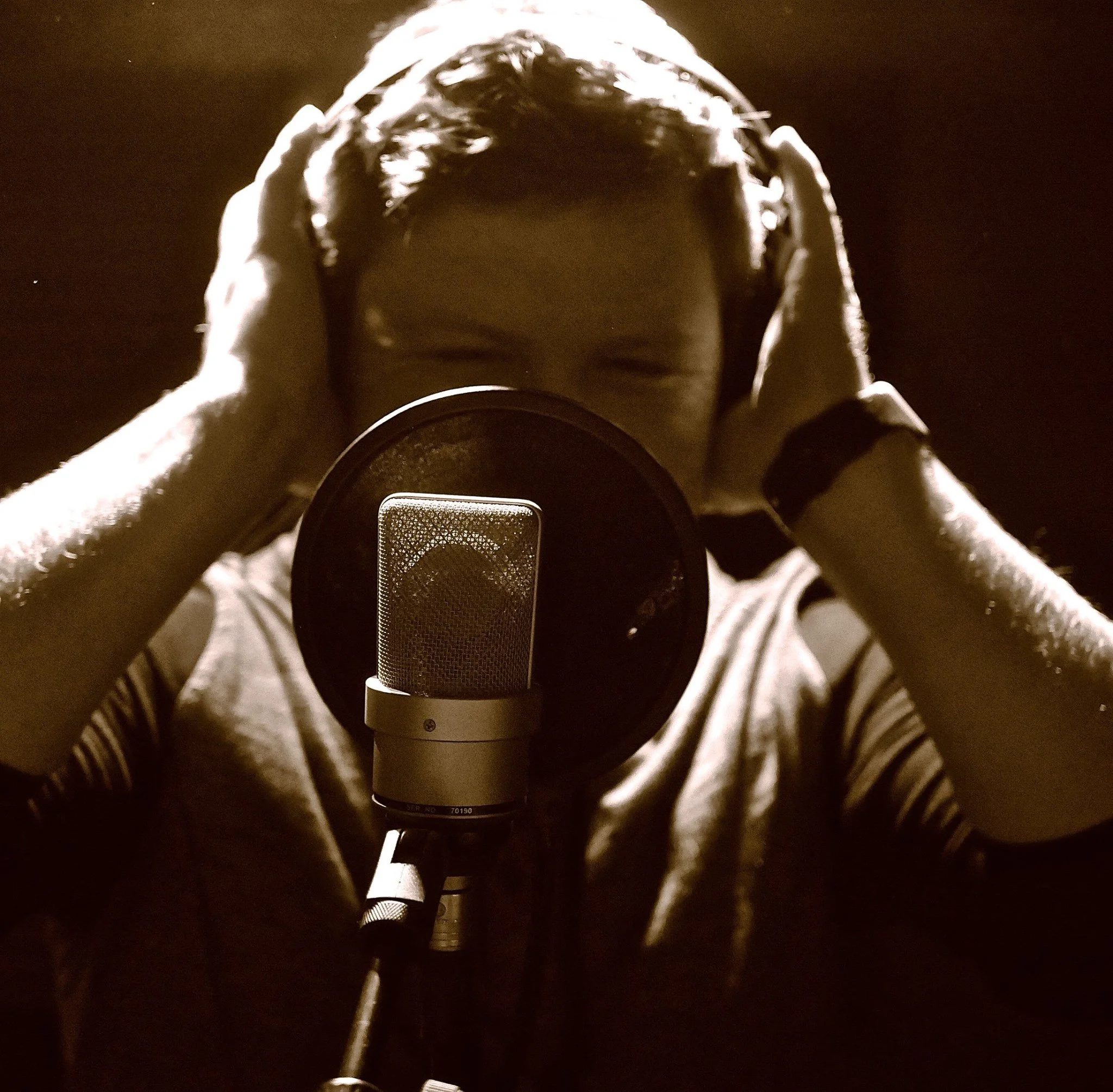 A person in a recording studio wearing headphones, standing in front of a microphone.