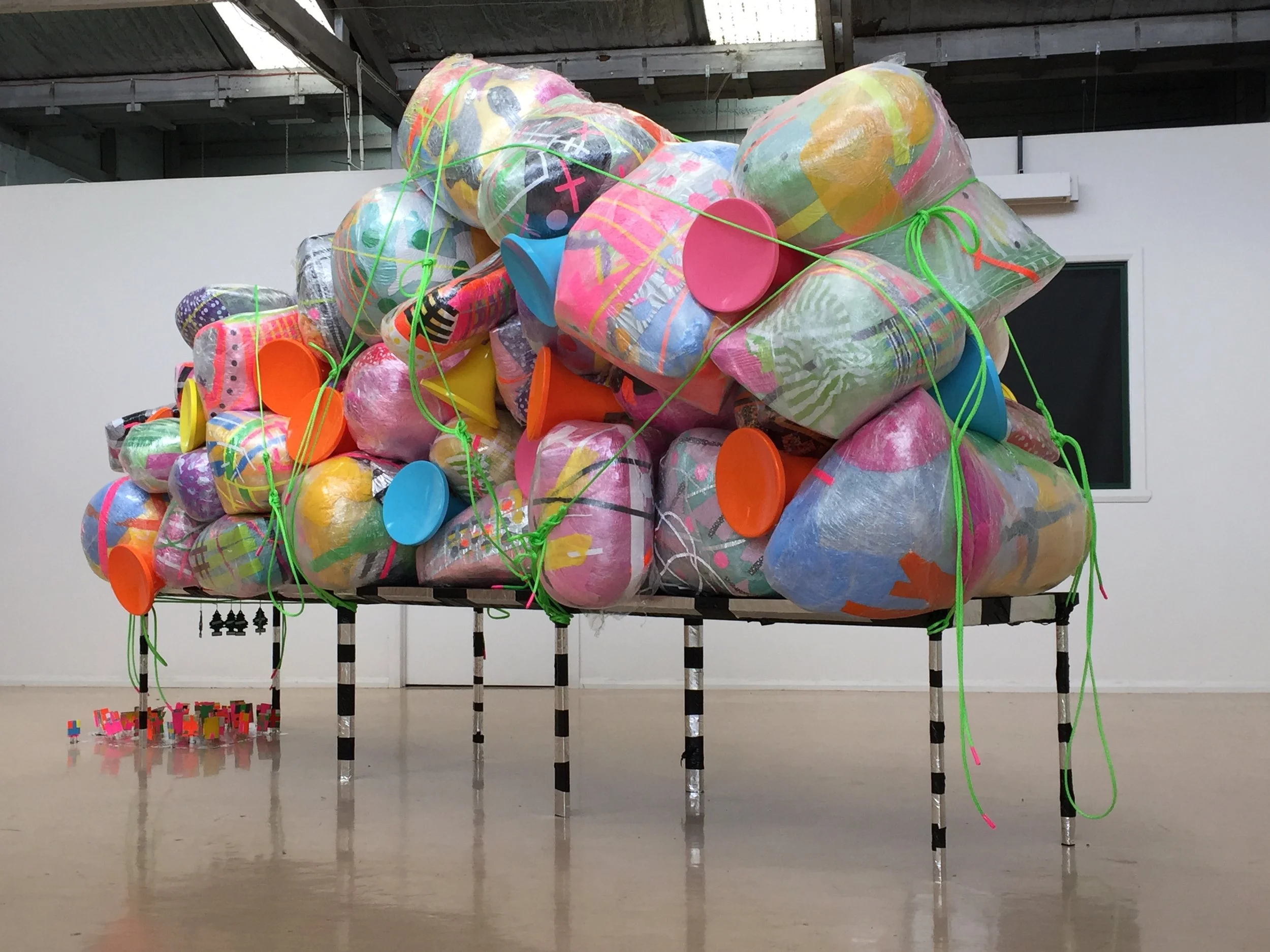 Pack - Proposition for an unstable minute, 2017.  Reclaimed plastic, cardboard, adhesive vinyl, tape, palette wrap plastic, rope, air fresheners and luggage ties on salvaged metal frame.  4500mm (H) x 7500mm (W) x 1800mm (D).