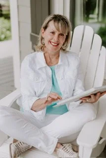 Smiling woman sitting on a white chair on a porch, reading a book