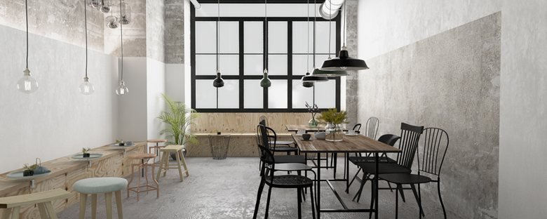Comedor industrial con mesa de madera, sillas negras y luz natural por una ventana grande.