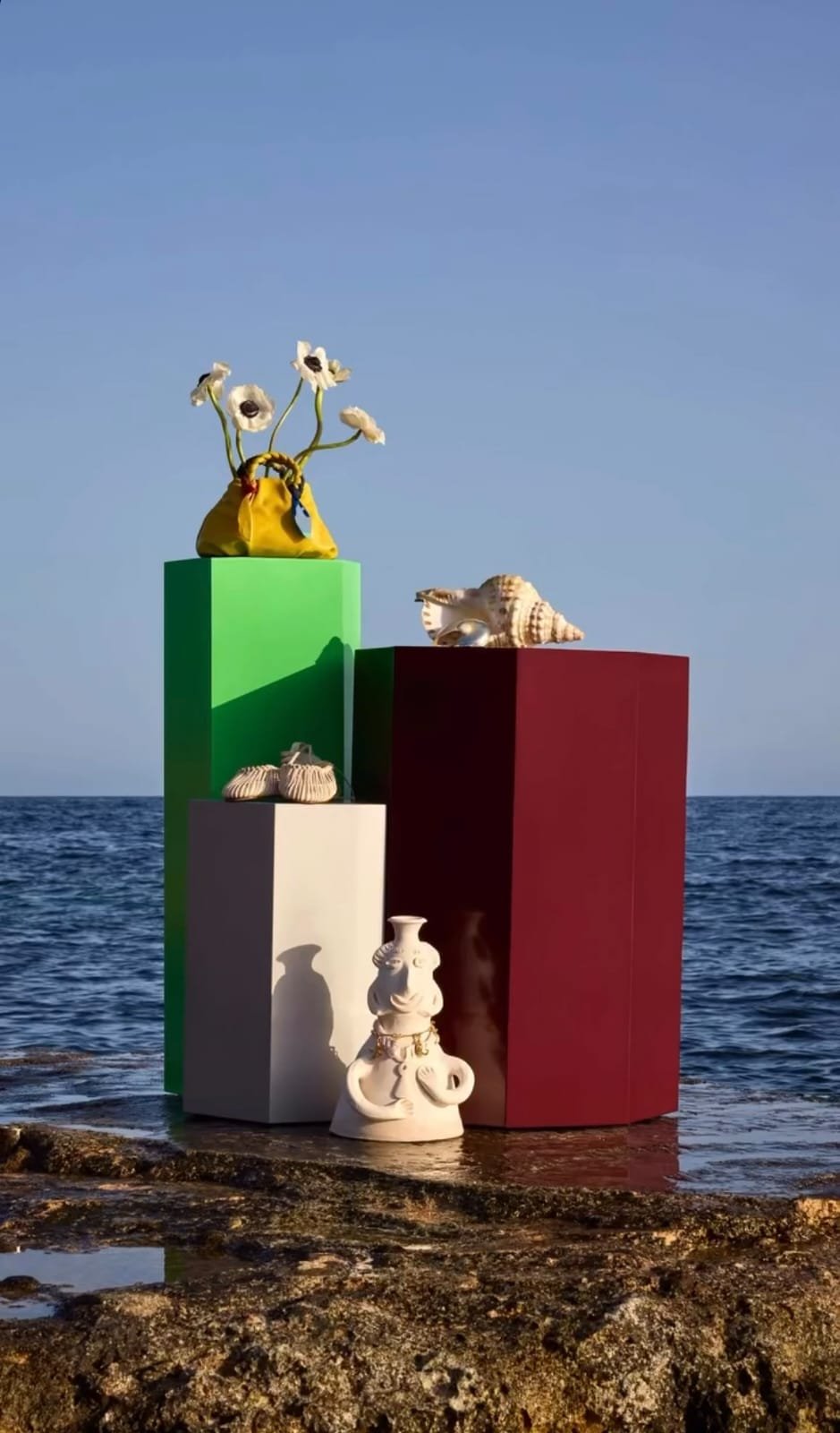 Estructuras de diferentes colores con objetos decorativos de conchas, cerámica y tela, situada junto al mar bajo un cielo despejado.