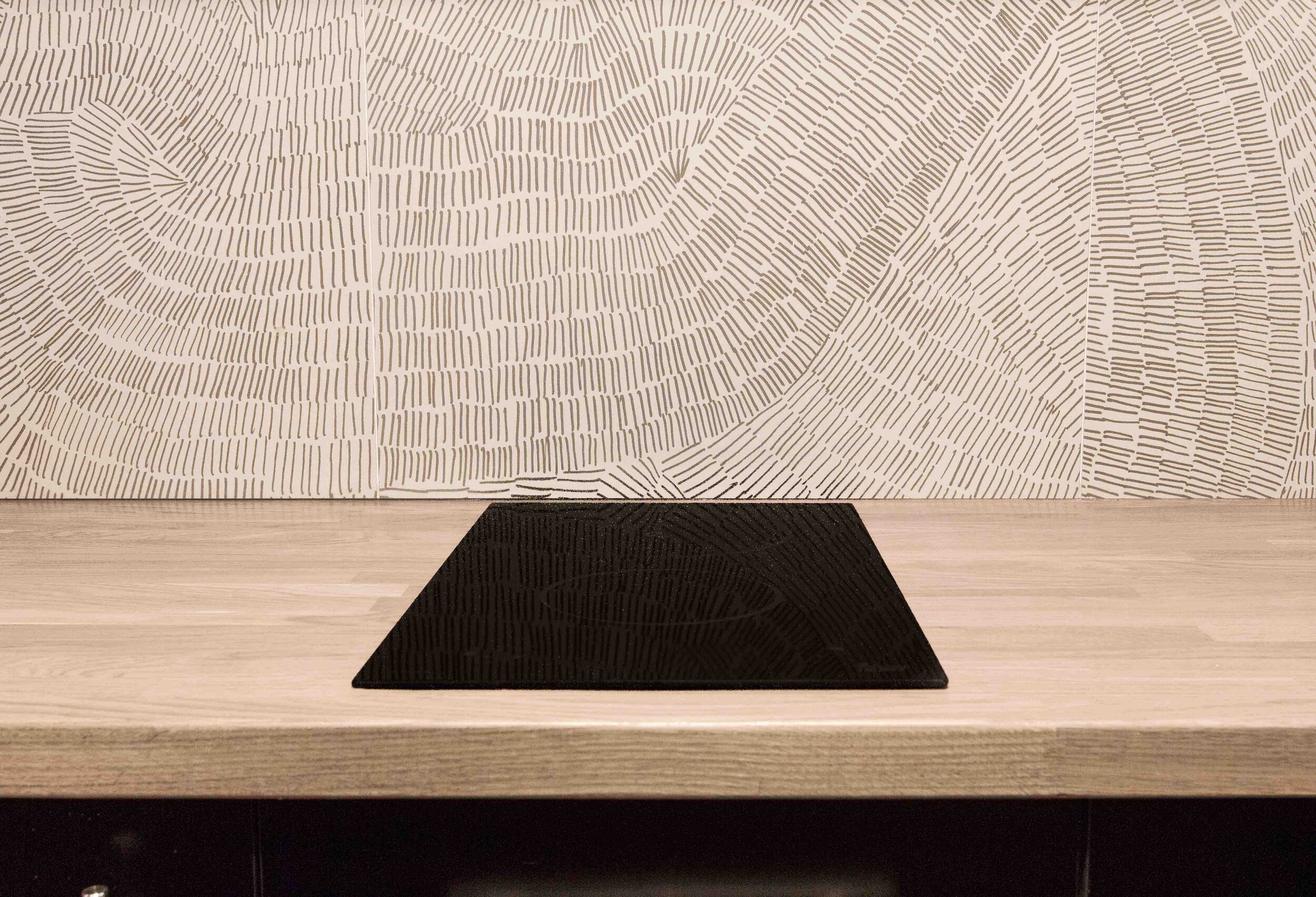 Piso de madera con una alfombra negra y pared decorativa con patrones lineales en tonos claros.