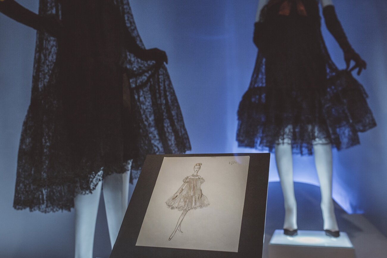 Dos maniquíes vestidos con vestidos de encaje negro y una ilustración de un vestido en un cartel en primer plano, en una exposición de moda.