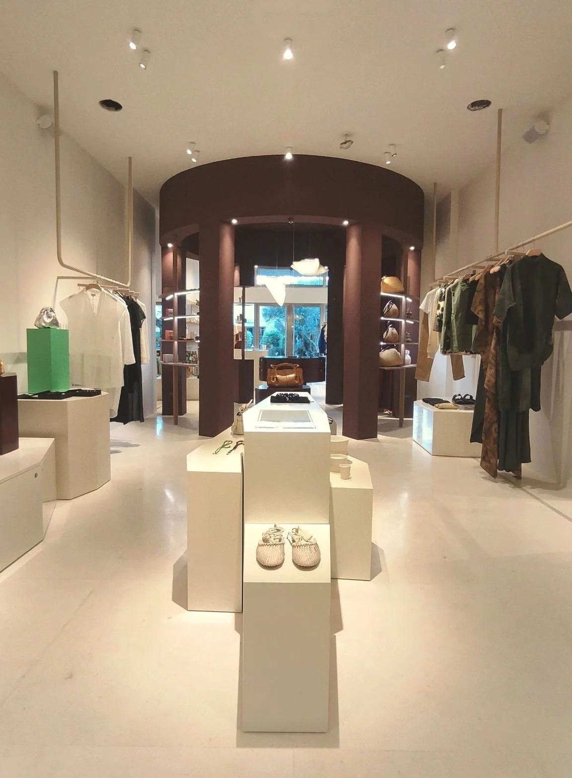 Vista interior de una boutique con ropa y accesorios en exhibición, paredes blancas y estructura de madera obscura en el fondo.