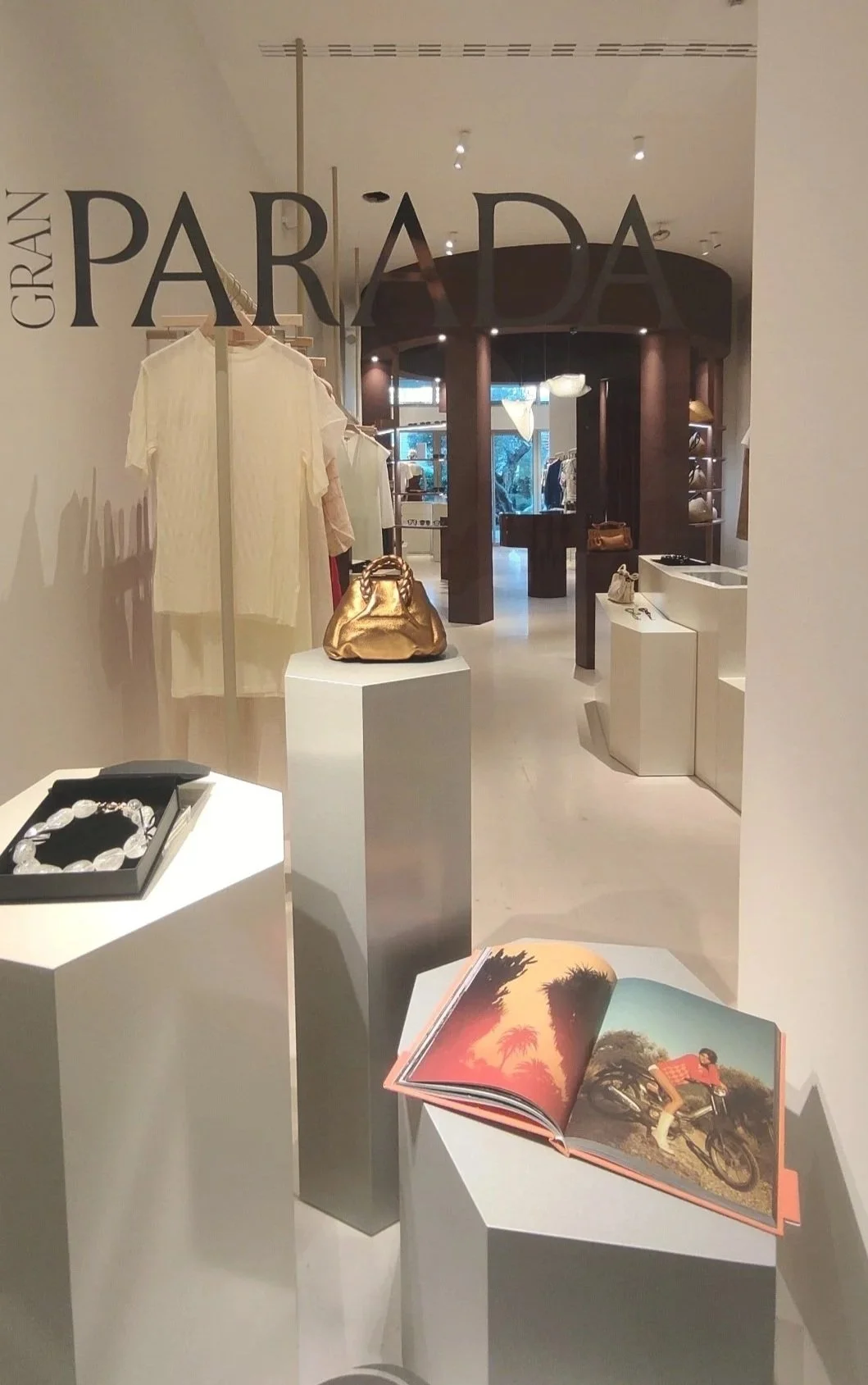 Vista de una tienda de lujo con exhibiciones de accesorios y ropa, visible a través de un cristal con letras que dicen "GRAN PARADA".
