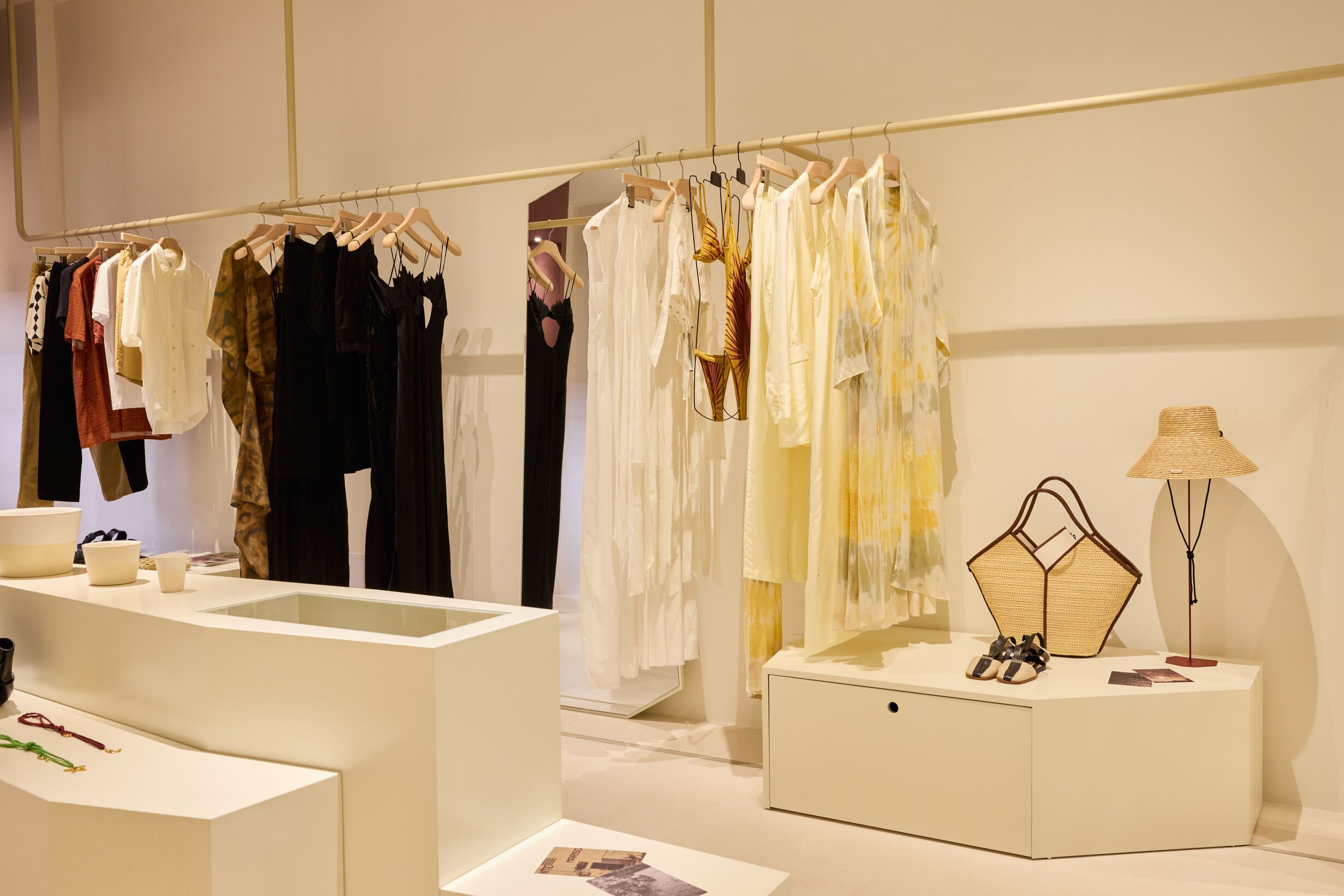 Ropa de verano y accesorios en una tienda de moda, colgada y exhibida en estantes y mesas blancas.