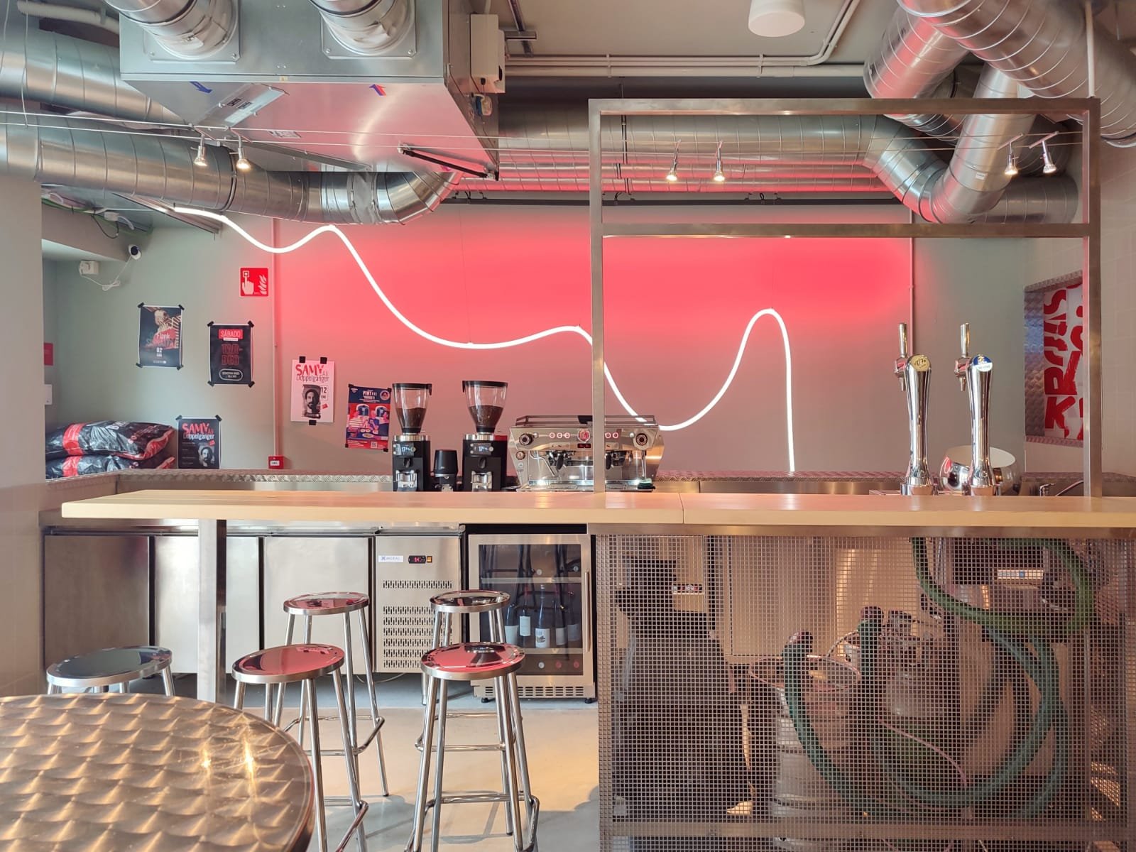 Bar de café con encimera de madera, mesas y sillas de metal, y decoración con luces de neón