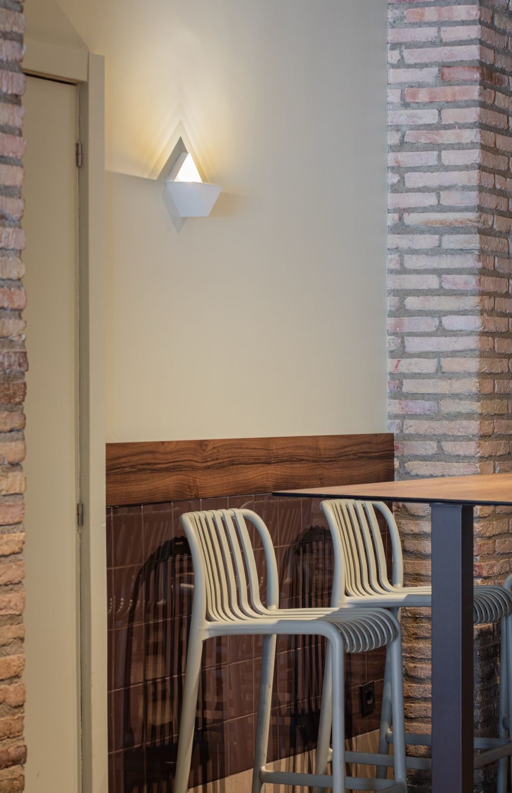 Mostrador de barra con sillas de plástico beige en un restaurante con paredes de ladrillo y una lámpara blanca en la pared.