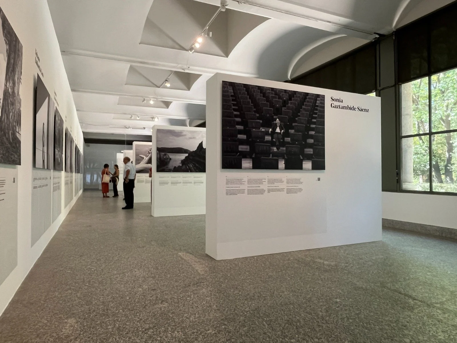Galería de arte con varias fotografías en exhibición y tres personas conversando.