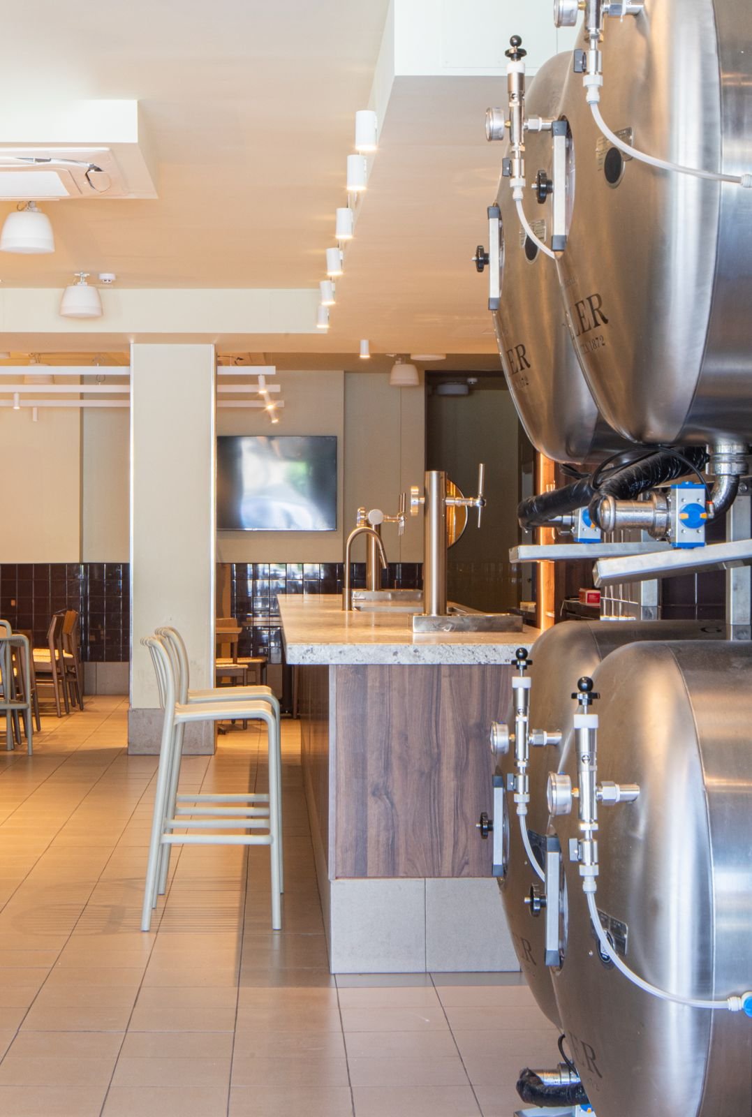 Interior de un restaurante con maquinaria de cerveza en un bar de madera y sillas en el fondo.