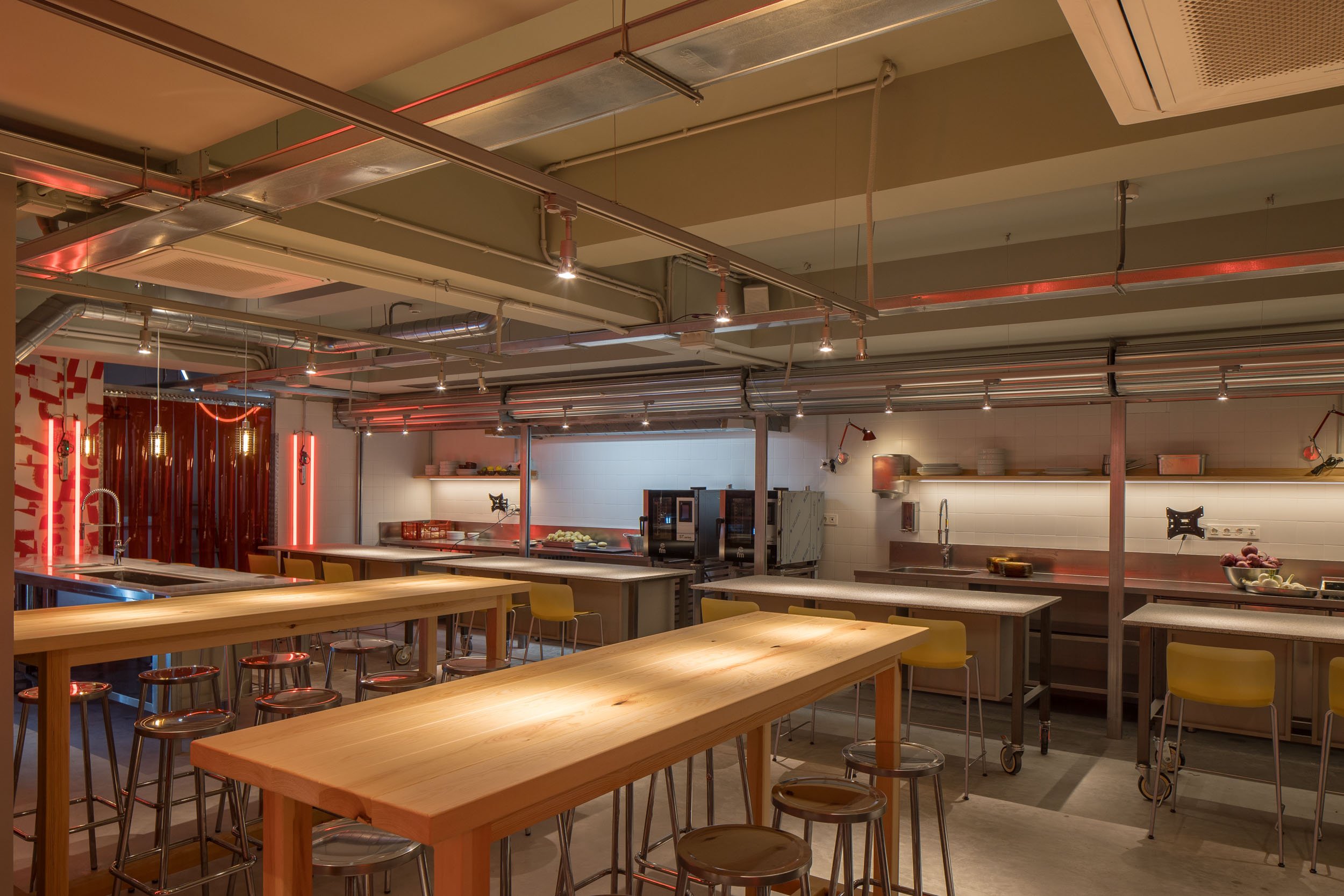 Interior de una cocina moderna con mesas de madera, sillas y estanterías con utensilios de cocina