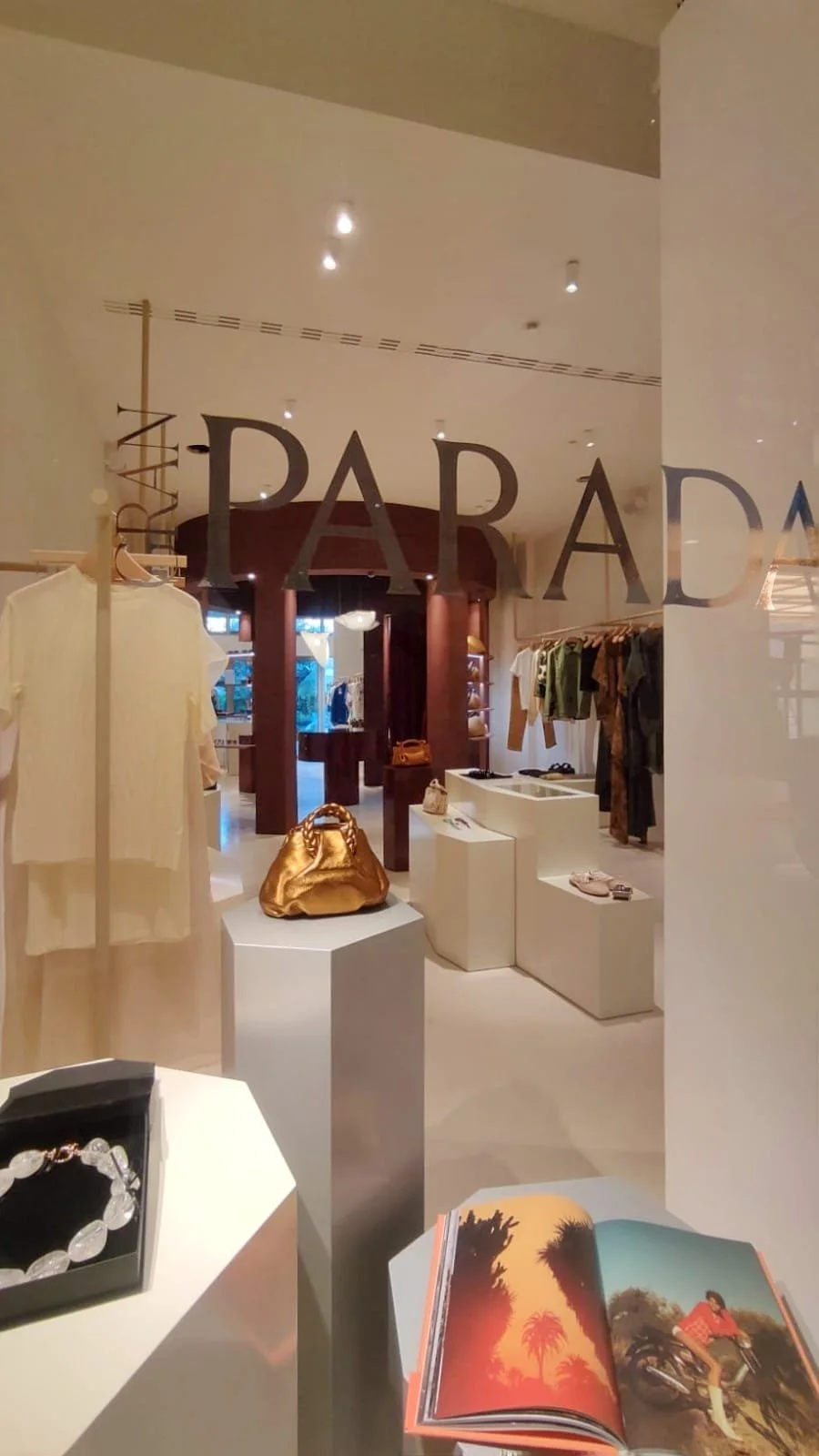 Diseño Vitrina de tienda de lujo con ropa y accesorios, visible el logo de Parada en la ventana, con una bolsa dorada sobre un pedestal. Interiorismo comercial