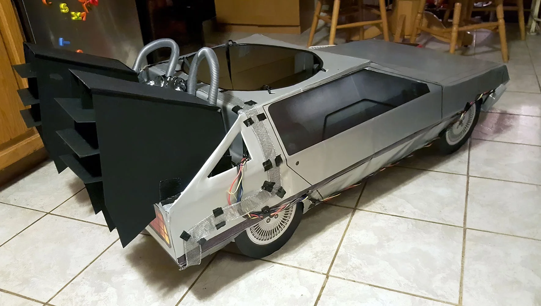 A partially assembled replica of the DeLorean time machine from the Back to the Future movies, on a tiled kitchen floor.