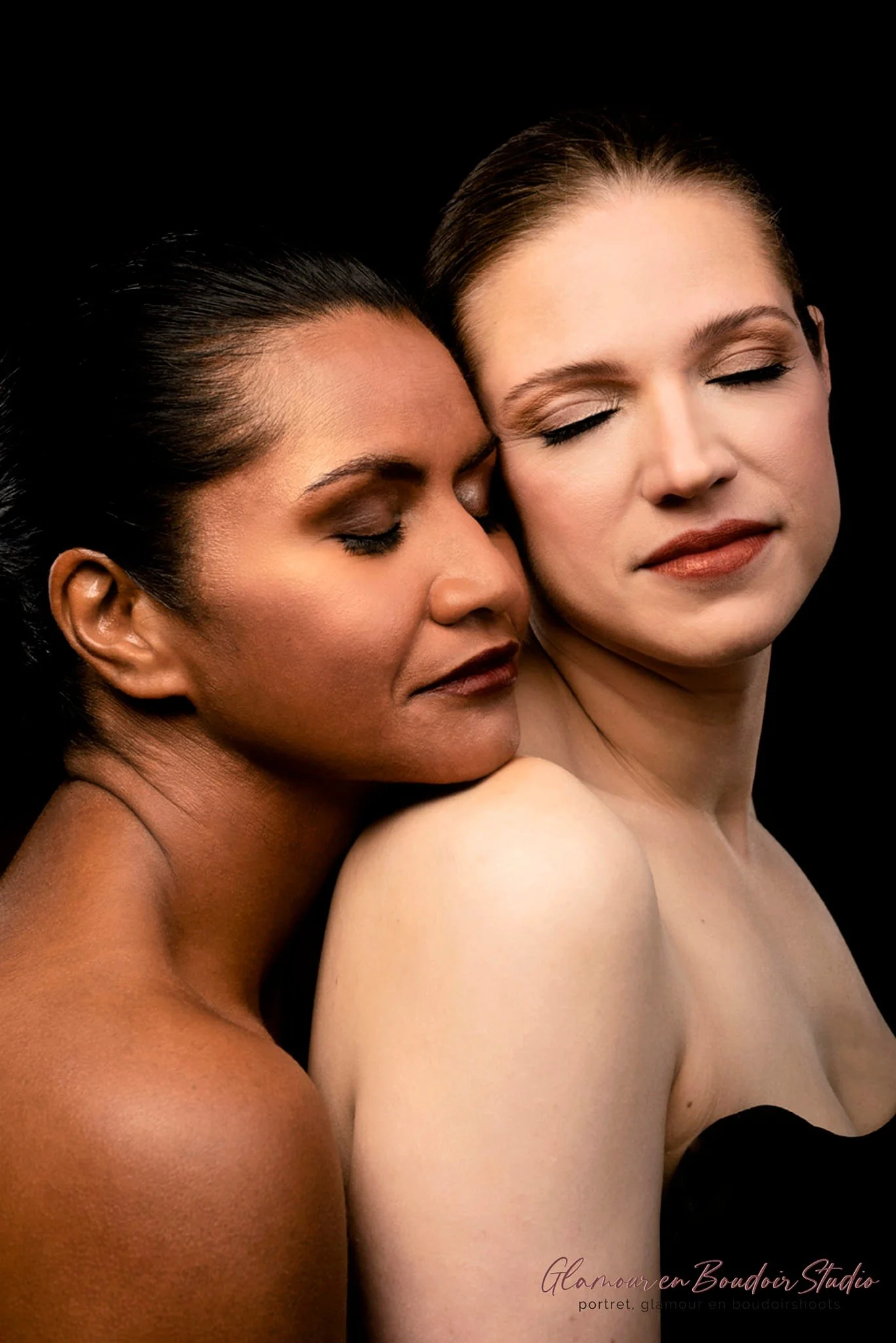 Two women with closed eyes and peaceful expressions, one with darker skin and the other with lighter skin, embrace against a black background.