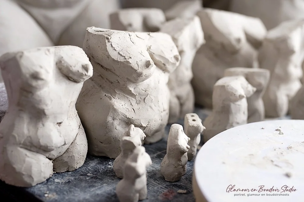 A collection of small, unfinished white clay or plaster sculptures resembling animals and abstract shapes, placed on a work table in an art studio.