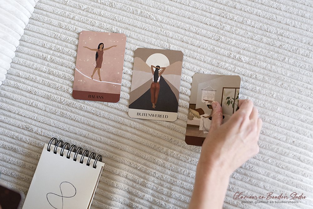 A person's hand flipping through tarot or oracle cards on a textured white surface, with a small blank notepad nearby.