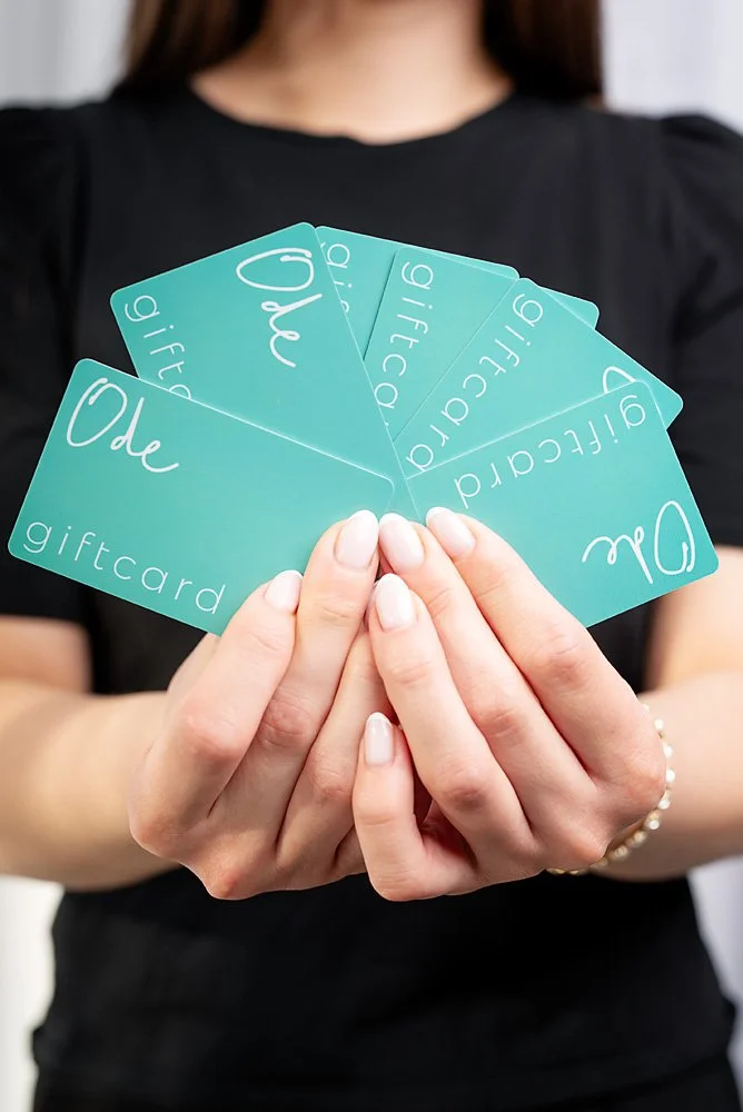 Person holding aqua-colored greeting cards labeled 'Ode,' 'Love,' and 'giftcard' in their hands.