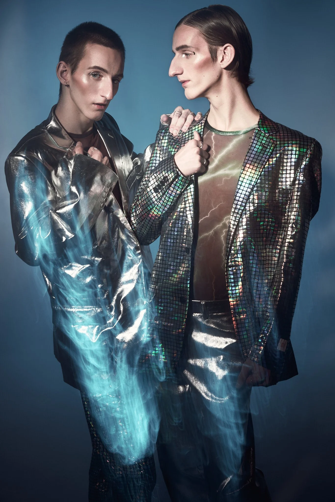 Half-length portrait of twin male models wearing reflective metallic jackets—one silver foil and one sequined checkerboard—under studio lighting.⁠