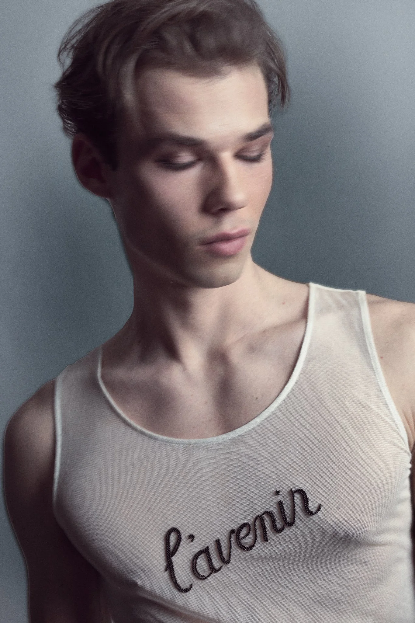 Soft, dreamy portrait of a male model wearing a sheer white Ann Demeulemeester tank top with “l’avenir” embroidered, photographed in studio with a painterly blur effect.