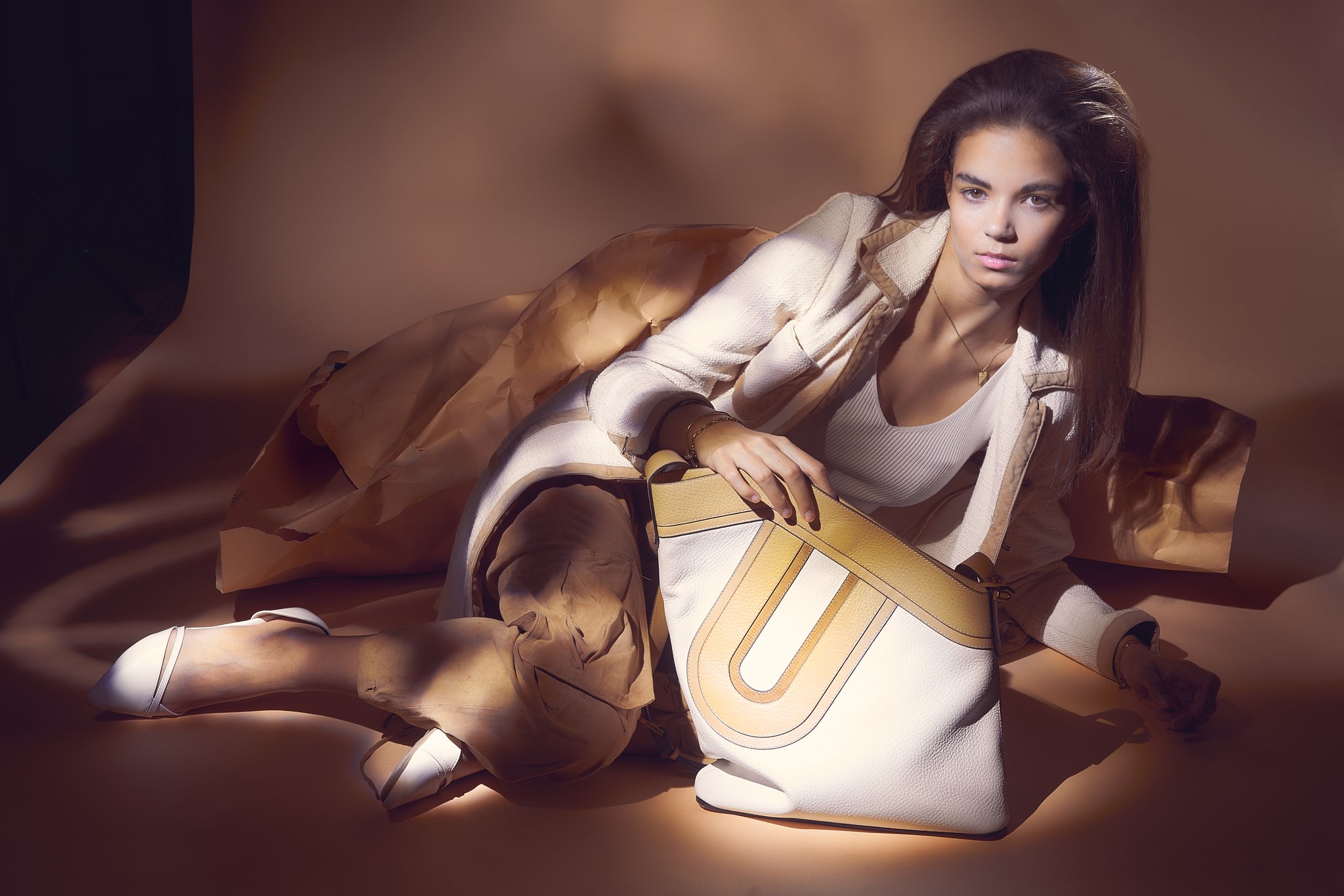Luxury leather shoulder bag campaign with reclining model, painted with light against a warm studio backdrop — premium commercial photography by Ghent-based fashion photographer Simon Rogghe.