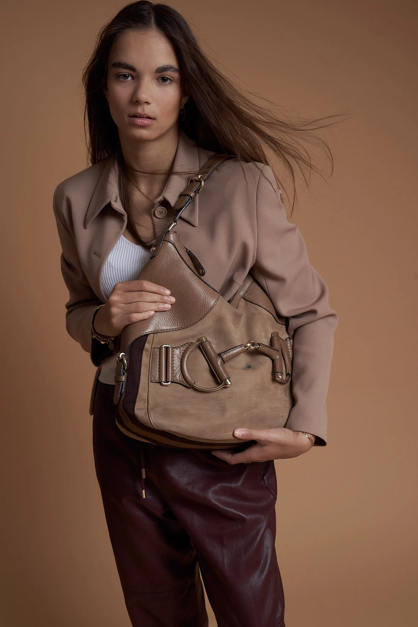 Fashion model standing in studio with beige textured coat, tan leather bag, and neutral backdrop — campaign-style product photography by Belgian fashion photographer Simon Rogghe.