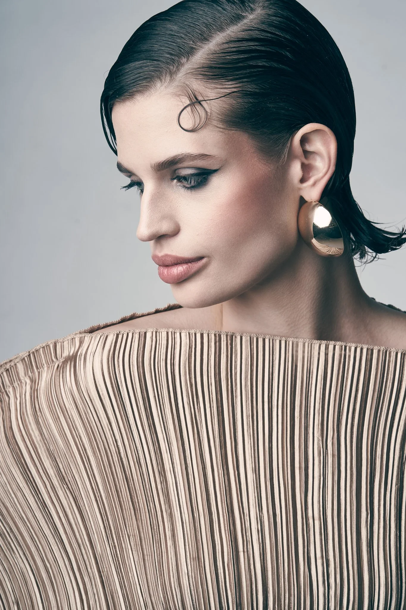 Profile portrait of a model with slicked finger-wave hair wearing a structured, high-neck beige pleated top.⁠